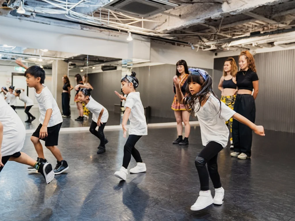 Young dancers perform a routine as their teachers watch