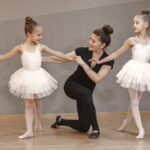 Dance teacher smiles and helps correct a young ballerina's form