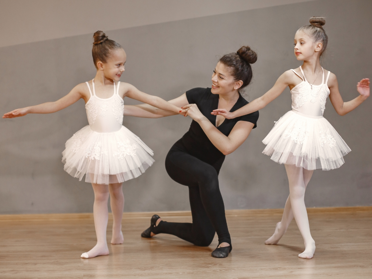 Dance teacher smiles and helps correct a young ballerina's form