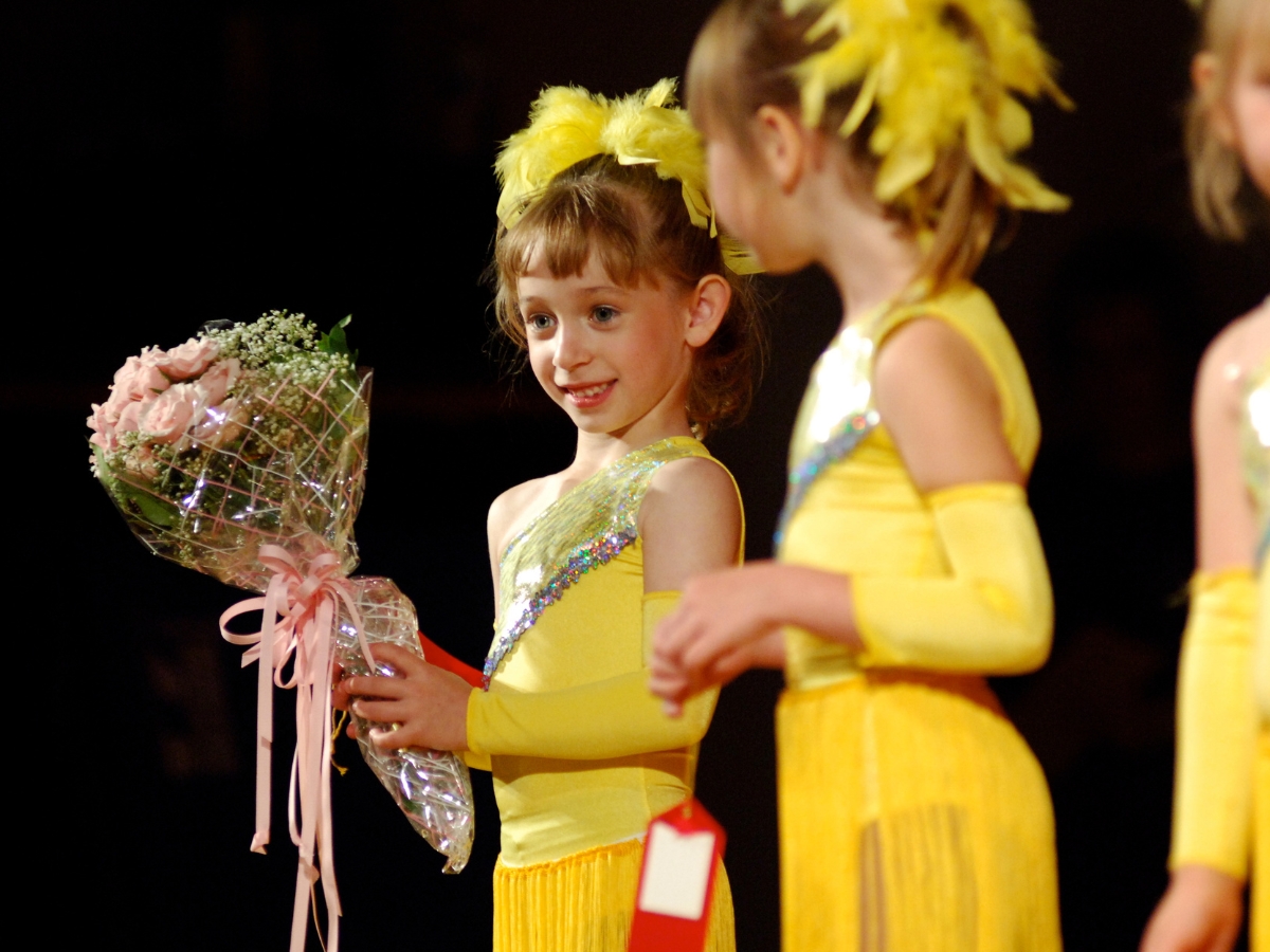 Young dancer holds a bouquet on stage in a yellow costume